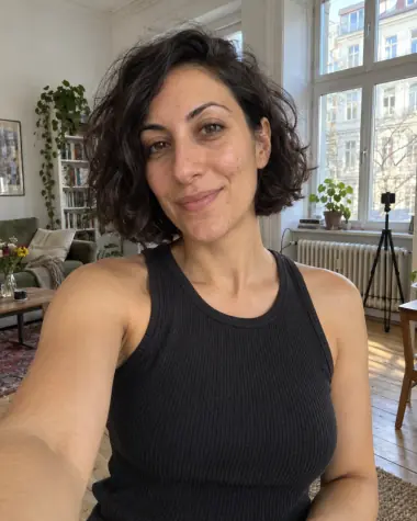 KI-Illustration einer erwachsenen fiktiven Creatorin beim Handy-Selfie in einer Berliner Altbauwohnung mit Stativ im Hintergrund.